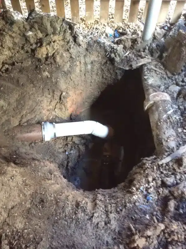 PVC drain repair joint inside a dug-out hole beside a fence