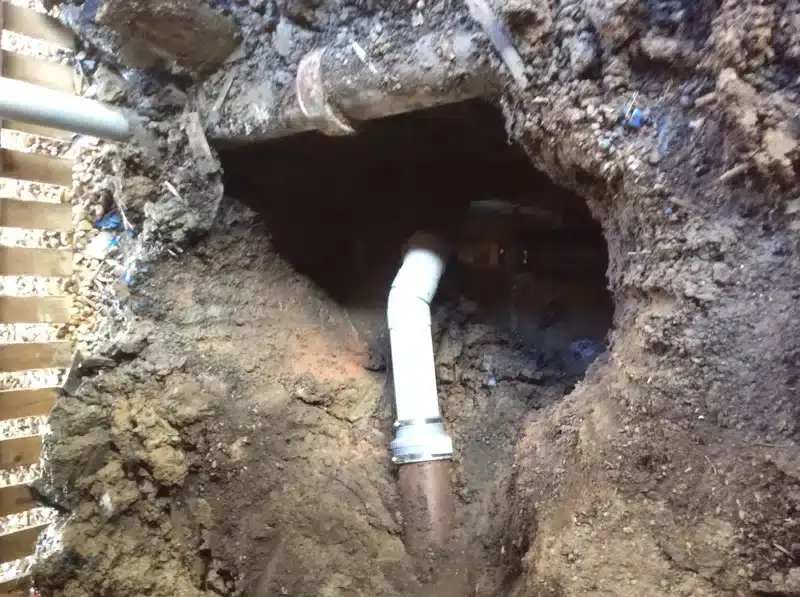 New white PVC bend joined to a clay drain in an excavation