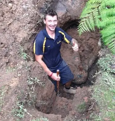 Bell plumber standing in a deep hole dug to reach a drain