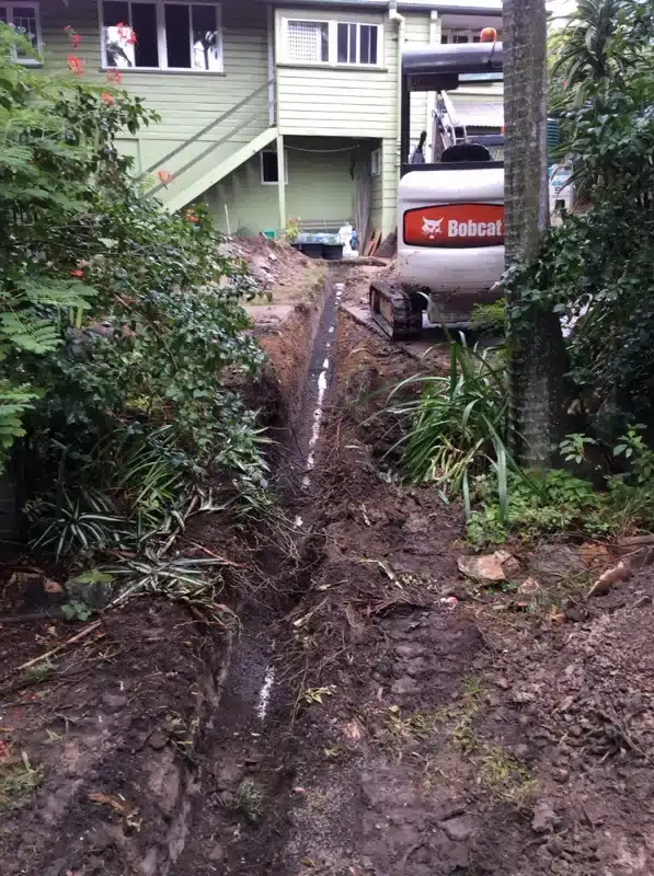 Trench for a new drain line dug by a small excavator along a garden