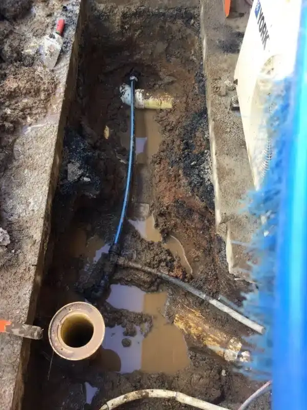 New section of water pipe laid in a muddy trench beside a pool