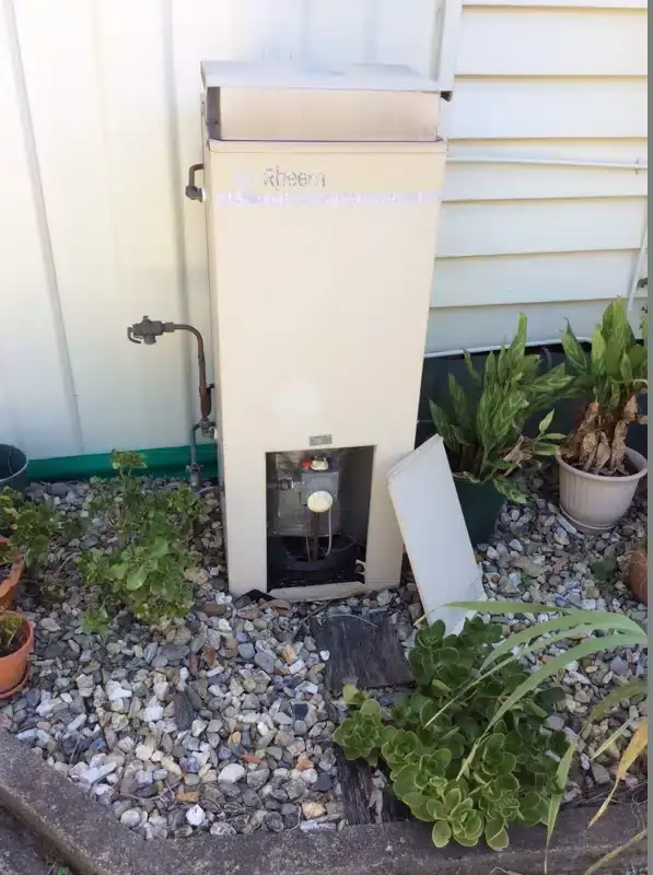 Old gas hot water unit on an outside wall beside a garden