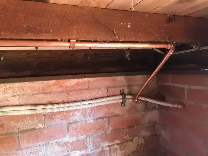 Copper water pipe and conduit fixed to a brick wall under a house