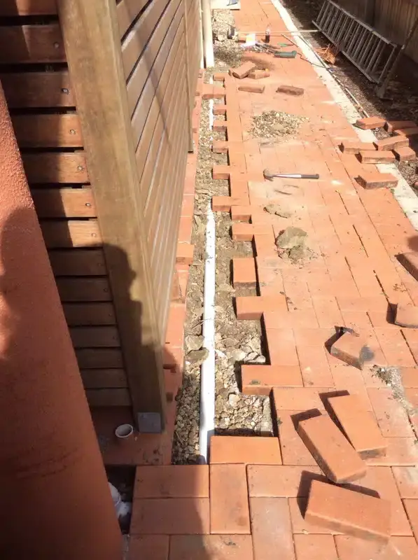 Brick paving lifted along a fence line for new pipework